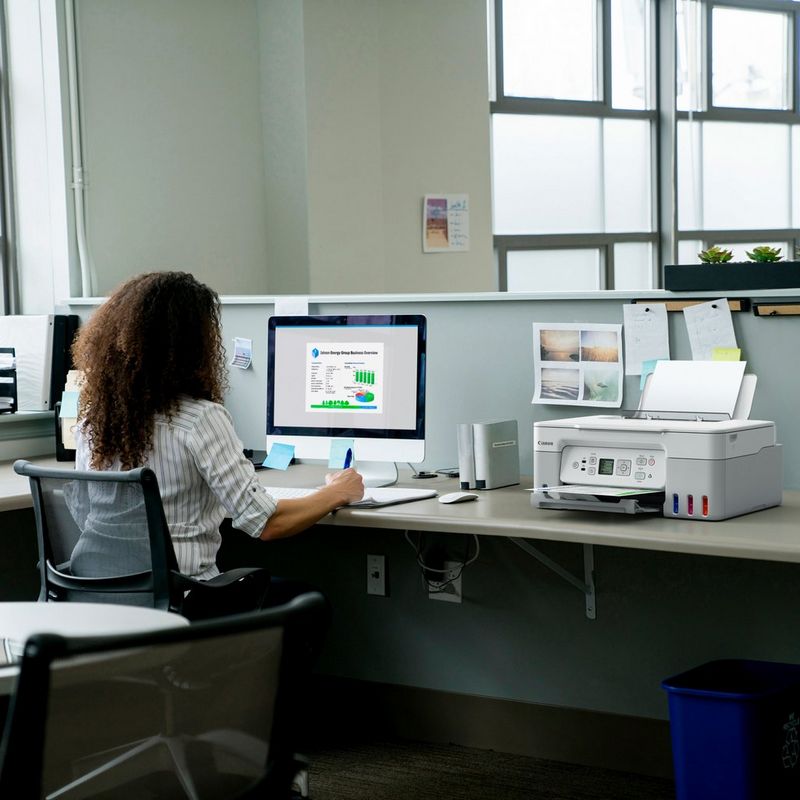 Canon PIXMA G3571 MegaTank 3-in-1 Farb-Multifunktionssystem mit WLAN und nachfüllbaren Tintentanks, Weiß Produkt auf einem Schreibtisch, an dem eine Frau an einem Computer arbeitet