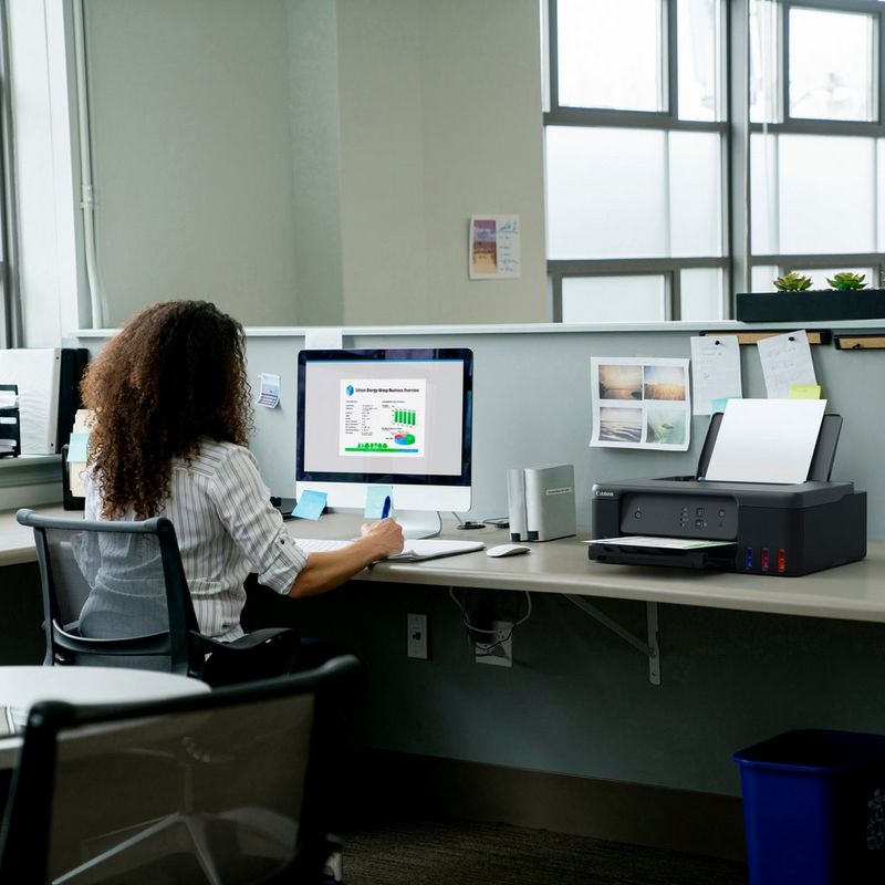 Canon PIXMA G1530 MegaTank Farbdrucker mit nachfüllbaren Tintenbehältern Produkt auf einem Schreibtisch, an dem eine Frau an einem Computer arbeitet