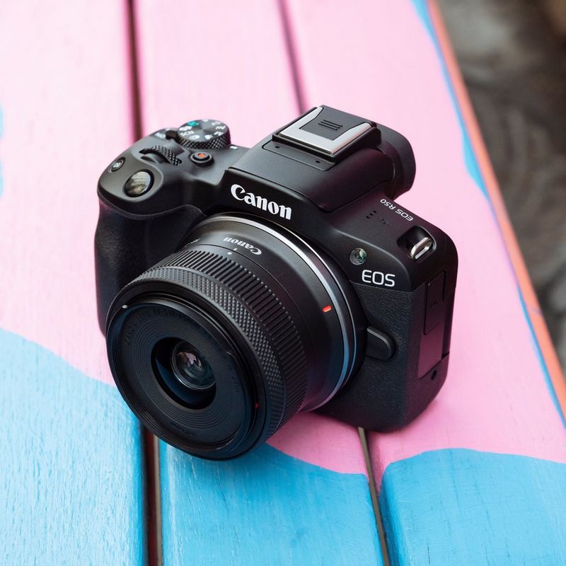 Canon EOS R50 spiegellose Kamera und RF-S 18-45mm F4.5-6.3 IS STM Objektiv Produkt auf einer blauen und rosafarbenen Bank