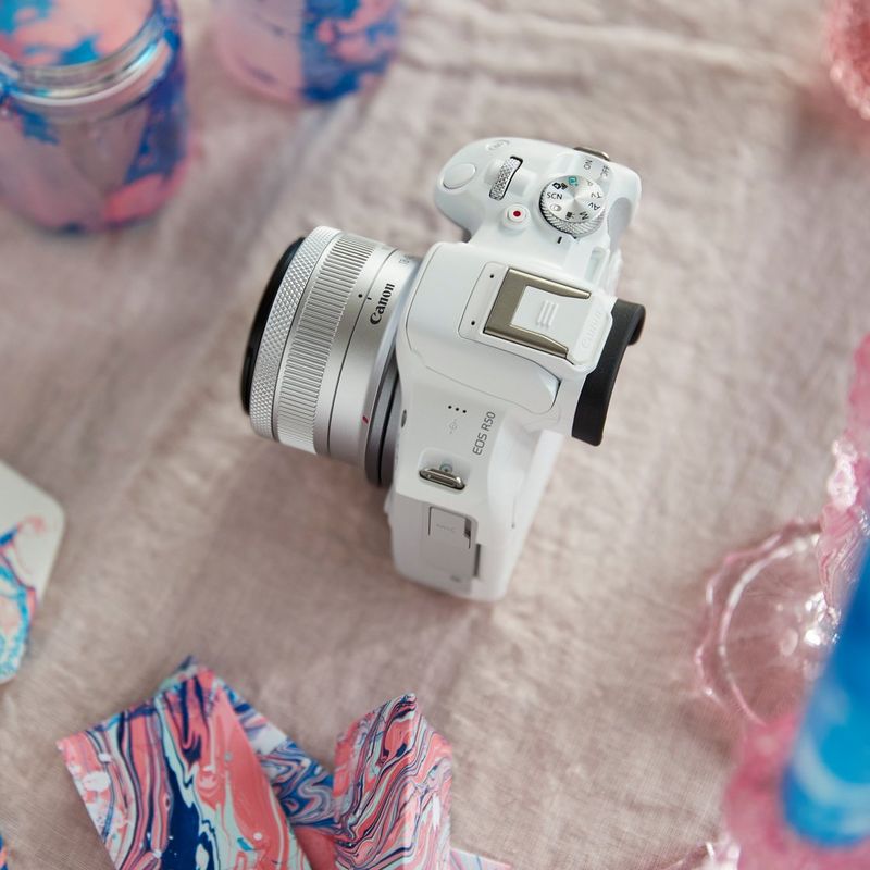 Canon EOS R50 spiegellose Kamera, Weiß und RF-S 18-45mm F4.5-6.3 IS STM Objektiv Produkt auf einem Tisch mit rosa Tuch