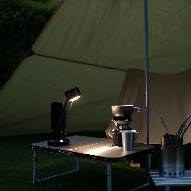 Canon Leuchte & Lautsprecher ML-A: drahtlose Bluetooth Lautsprecher Lampe aus Aluminium - Schwarz Produkt mit gekipptem Arm und eingeschalteter Lampe in einem Zelt