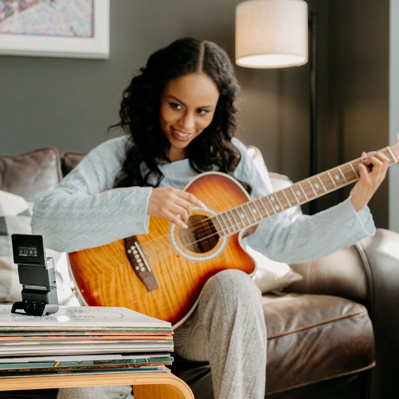 PowerShot-V10 Frau, die Gitarre spielt und einen Vlog aufnimmt, wobei das Produkt mit aufgeklapptem Display auf einem Tisch steht