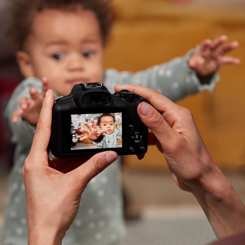 Canon EOS R100 spiegelloses Kamera Frau, die sich ein Baby durch das Produktdisplay ansieht