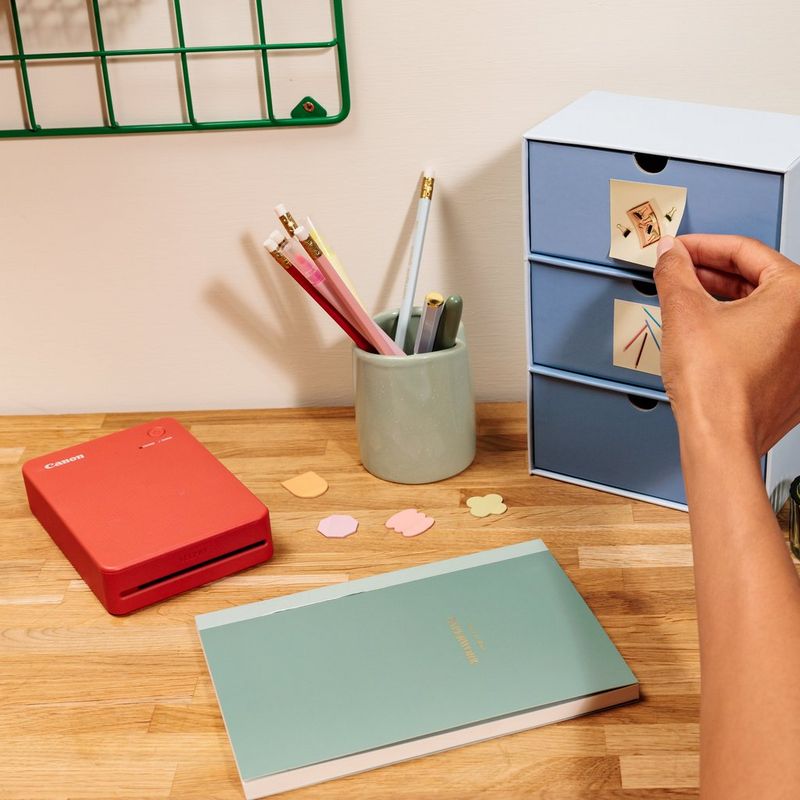 Canon SELPHY QX20 mobiler WLAN-Farbfotodrucker, Terrakottarot Produkt mit gedruckten Fotos, die an einem Schrank kleben