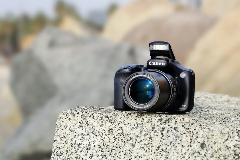 Canon PowerShot SX530 HS Vorderansicht der Kamera mit ausgeklapptem Blitz auf einem Felsen