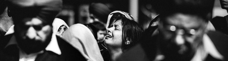 A woman, surrounded by men at a cremation in India, raises her head to the sky and cries