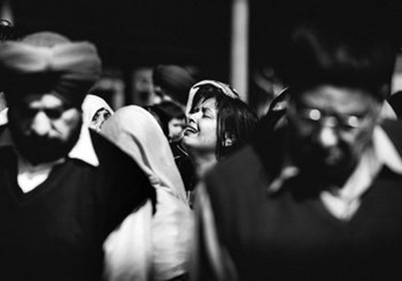 A woman, surrounded by men at a cremation in India, raises her head to the sky and cries