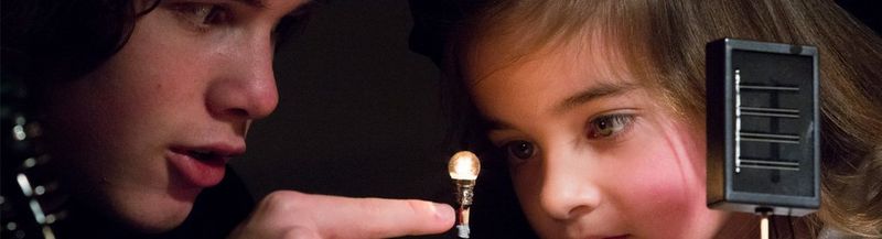 A boy points at a lightbulb, as a small girl watches closely
