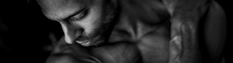 An artful portrait of a man in black and white. He has his hand on his shoulder and a light beard.