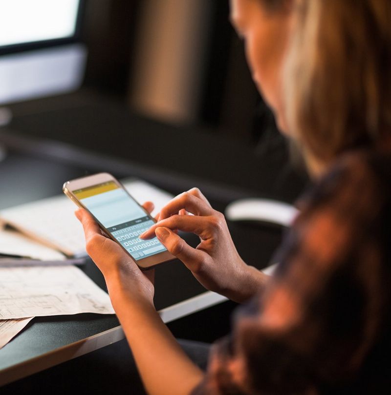 Looking down on four people sitting on orange and black chairs around a table covered in laptops, tablets and papers.