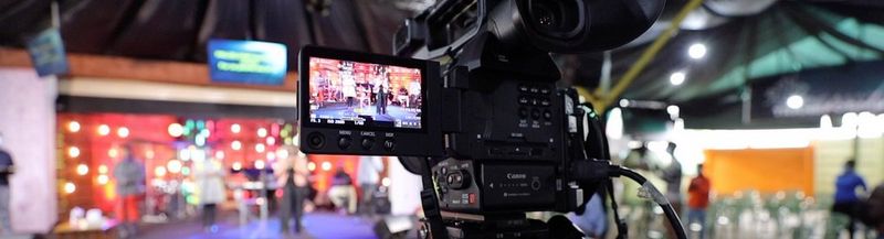 A close up of the back of a Canon EOS C100 Mark II camera as it films a stage that is blurred in the shot, but clear on the viewfinder.