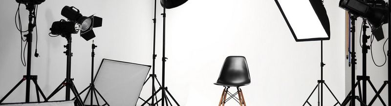 A black chair in the middle of a white photography studio, surrounded by lights.