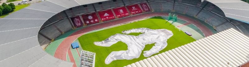 An aerial view of the King Baudouin Sports Stadium in Belgium, with a huge image of a figure wearing a silver fire-resistant suit laid out across the pitch.