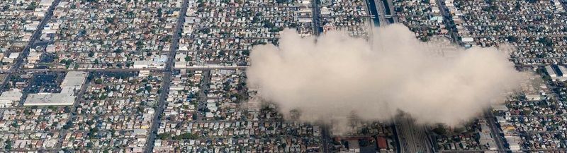 An aerial view of a city with a large white fluffy cloud above it on the right-hand side.