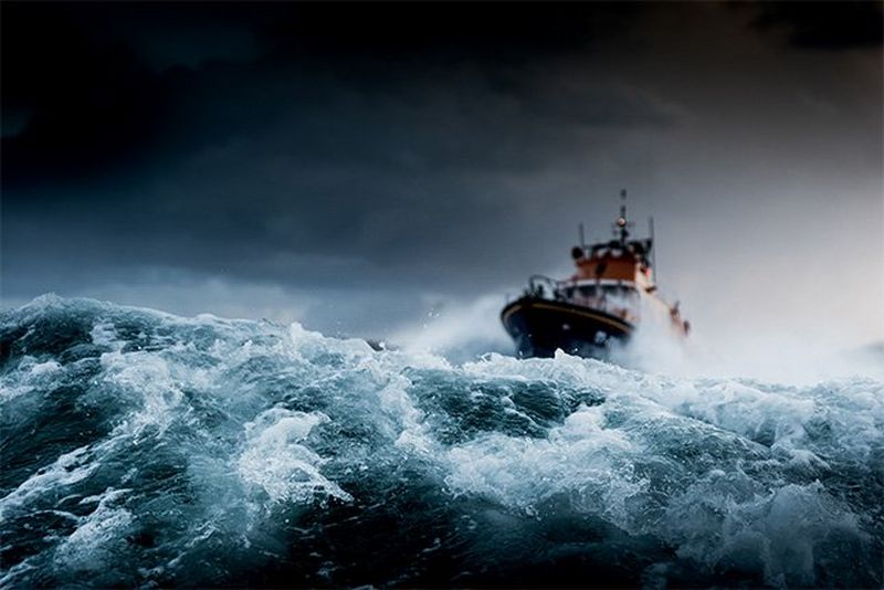 In the foreground is a swell of rough sea, while in the background a lifeboat approaches.