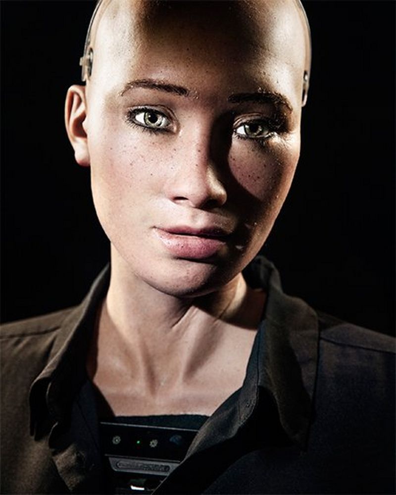 A close-up of Sophia's face and neck. She wears a black top and is lit to show strong contrast with bright highlights and dark shadows.