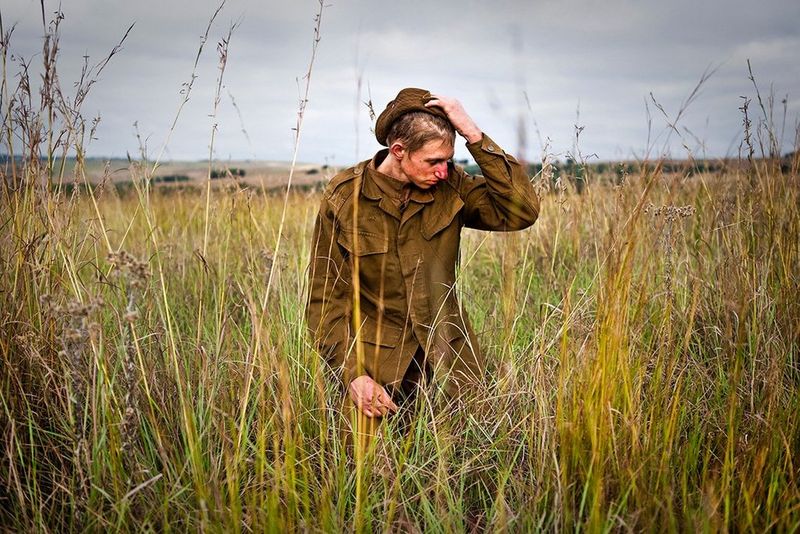 A group of white Afrikaans teenage boys wear army uniforms and stand in a group in front of an army tent, under a starry night sky.