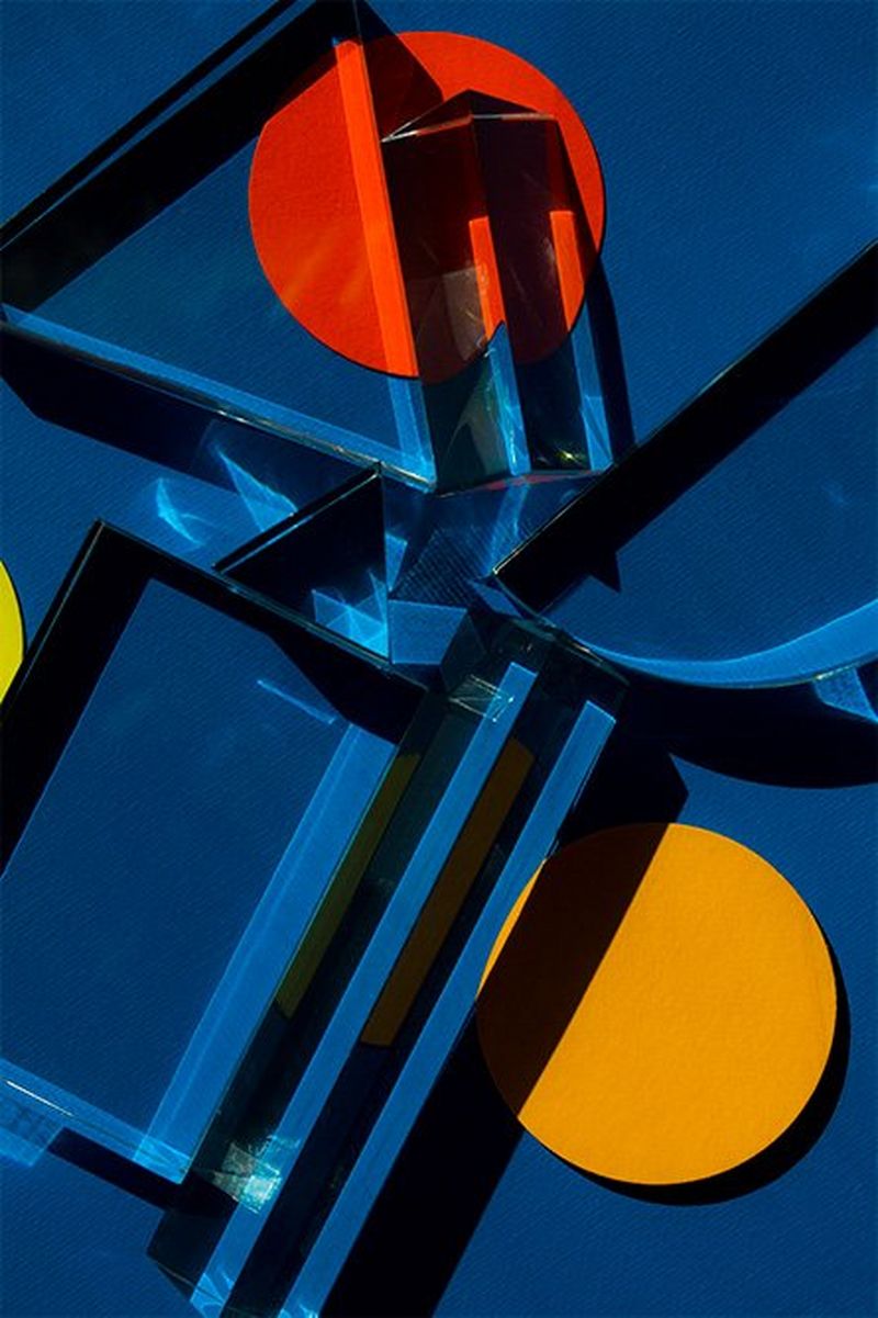 A close-up of a mysterious, brightly-coloured object with circles and sharp edges casting shadows. The colours are mainly rich blue with red and yellow circles.