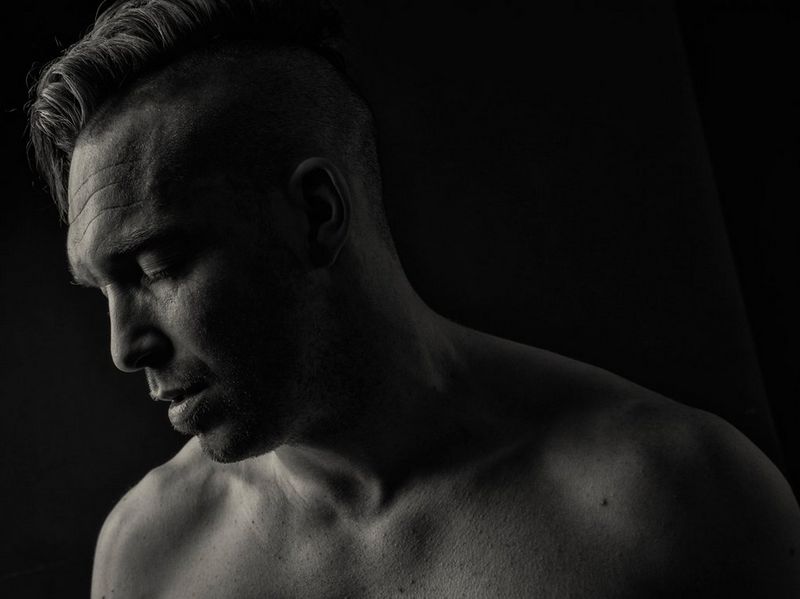 A black and white headshot of wrestler Jack Sexsmith, with bare torso, head tilted forwards and eyes closed.