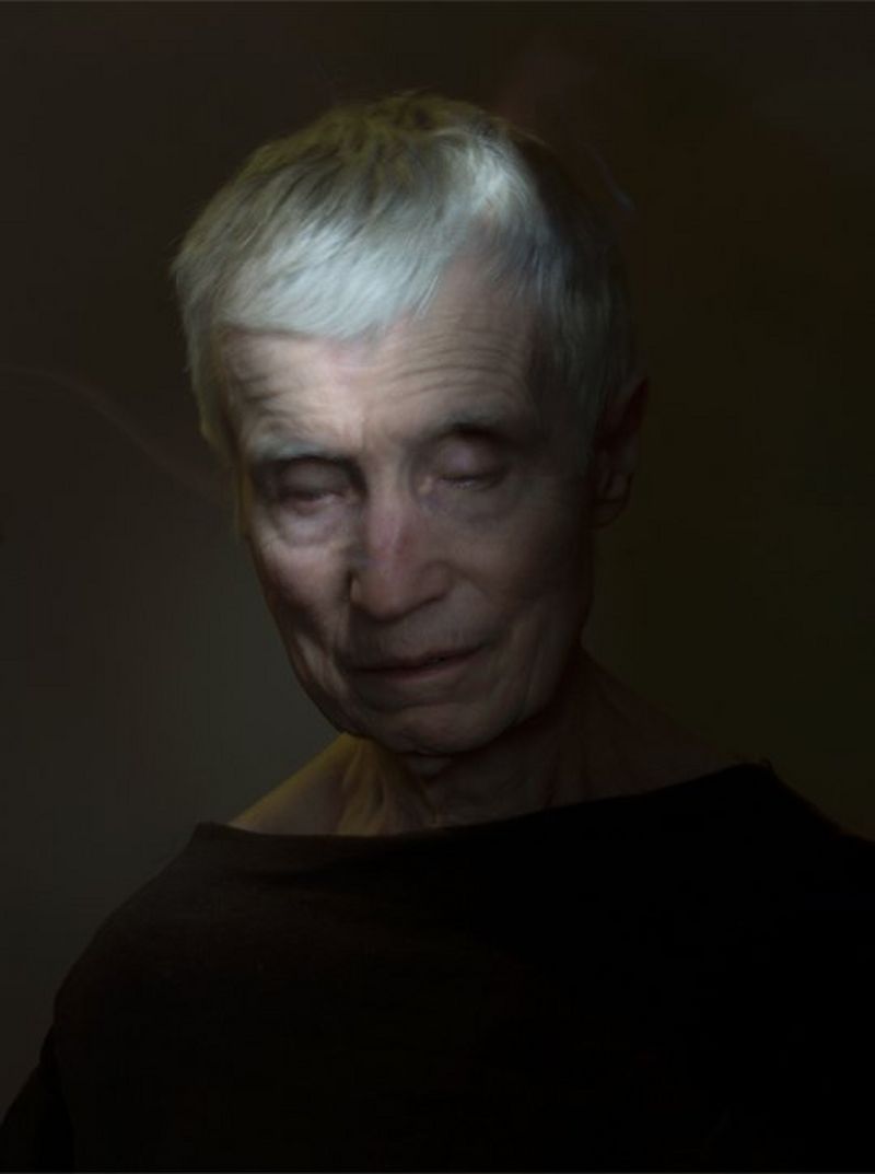 A portrait of a white-haired woman. The lighting is dim, and her head is tilted downwards.