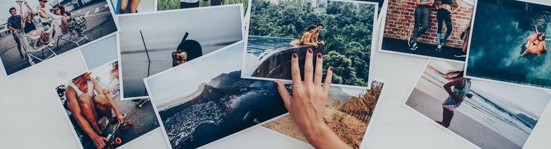 An assortment of photos laid flat. The right hand of an unseen person lays across three photos in the centre of the image.