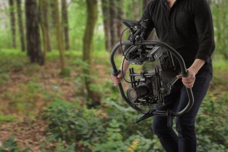 A man holding an EOS C500 Mark II on a gimbal, filming in a forest.