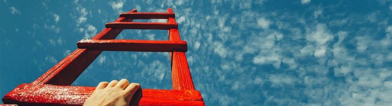A hand reaching onto a red ladder, which points at a bright blue sky