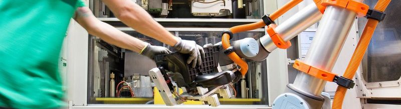 A man on the left and a robot arm to the right, both holding the same object 