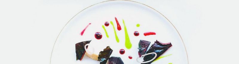 A red chard, beetroot, plant ricotta and parsley dish. Only the top half of the gold-trimmed white plate is shown and sits as a semicircle in the middle of the photo. The sauces of the dish are spotted and striped on the plate in bright pinks and vivid lime green.