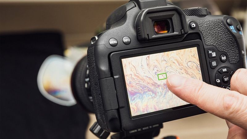A person tapping the screen of an EOS camera. 