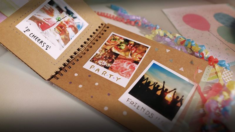 A Canon SELPHY SQUARE QX10 in front of a book full of pictures.