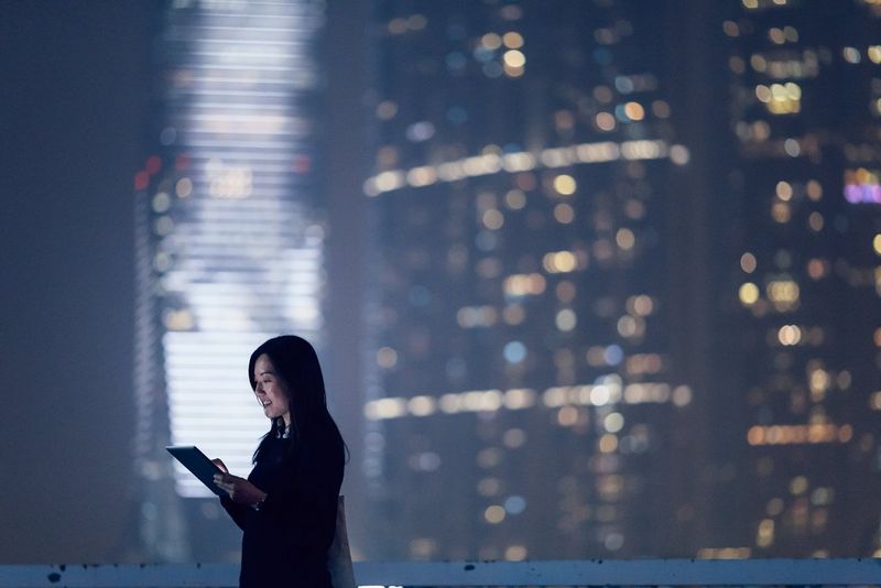 Woman on tablet at night in front of blurred building and lights