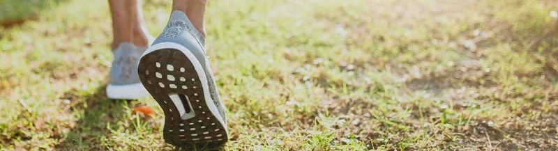A pair of feet in running shoes, walk across grass.