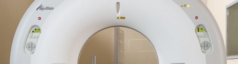 A white, half-doughnut shaped machine, which is a partial view of a Canon Medical Aquilion LB CT Scanner. It has operating buttons on either side of the central gantry.