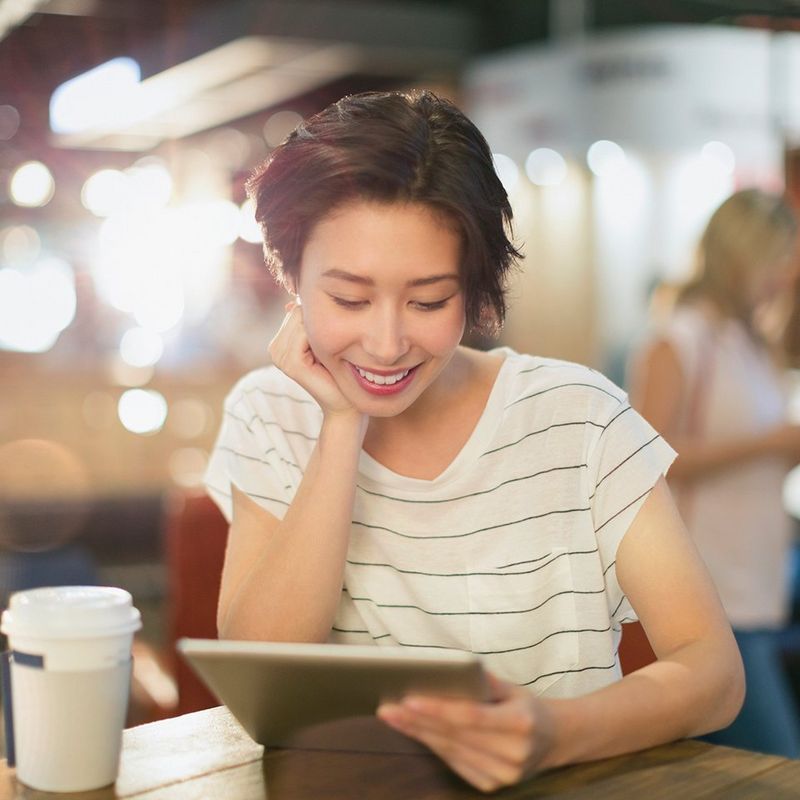 Young woman using digital tablet and drinking coffee