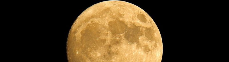 A large, yellow supermoon against a black sky