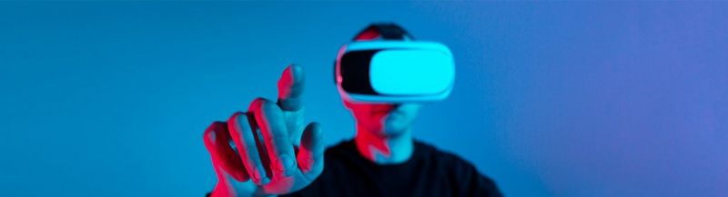A man in a VR headset stands against a blue background with his finger pointed to the camera.