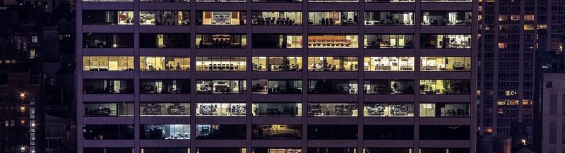A building, photographed from the outside at night, showing dozens of lit offices.