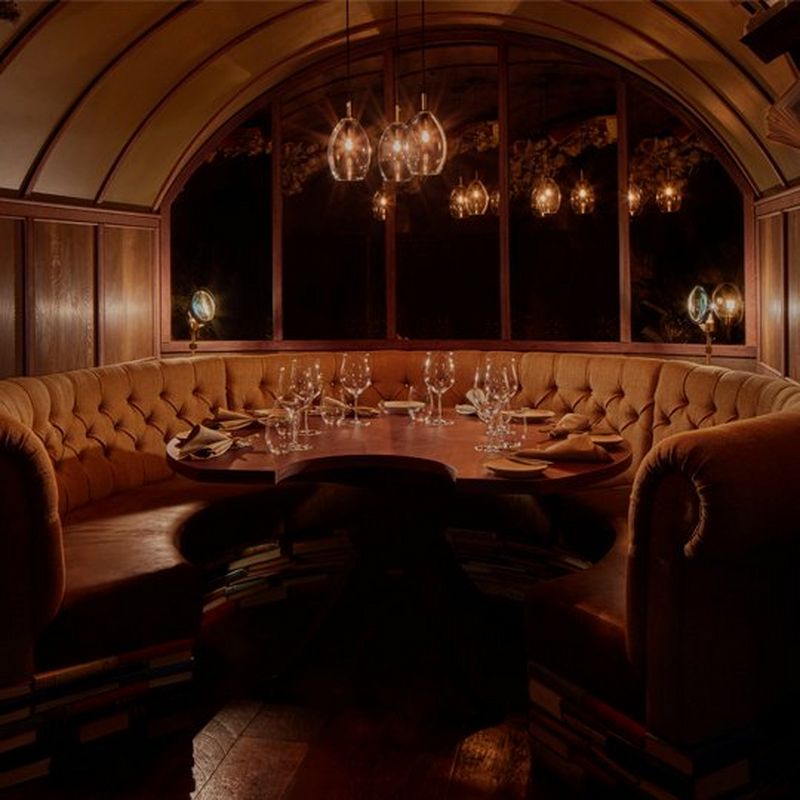 A small, dimly lit, private dining room with seating in a semi-circular booth ad wood panelled walls.