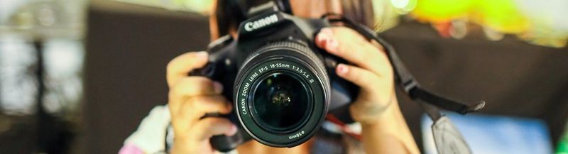 A child holds a Canon camera, obscuring his/her face