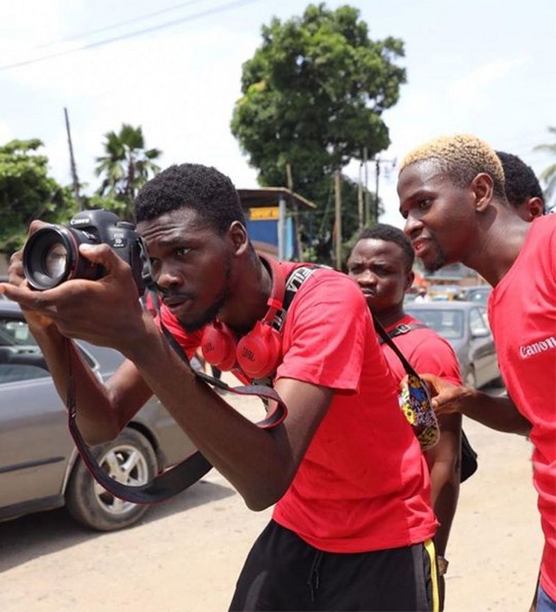 Four young men, one holding a camera, look carefully at the shot they are about to take.