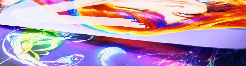 The edges of two colourful printed posters, laid one on top of the other. One is a woman’s face with rainbow coloured hair. The other is an illustrated night scene in the fantasy style of purples and neon brights.