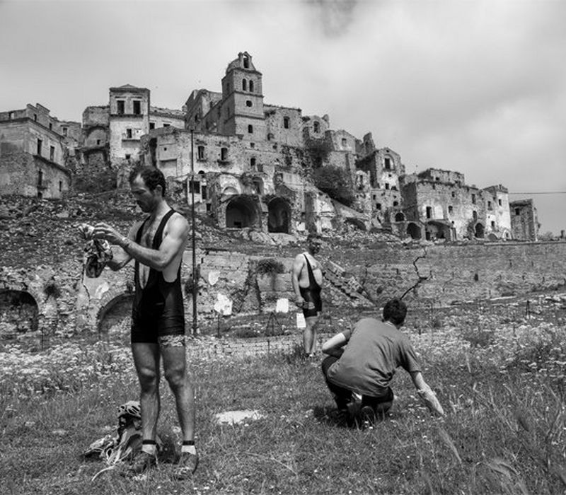 A black and white image of three men in lycra, standing in front of the buildings of Sassi di Matera. 