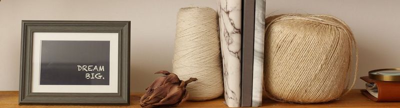 A shelf with, left to right: a picture frame containing the quote ‘dream big’, a dried flower, a ball of thread, a notebook, another ball of thread and the edge of a leather organiser.