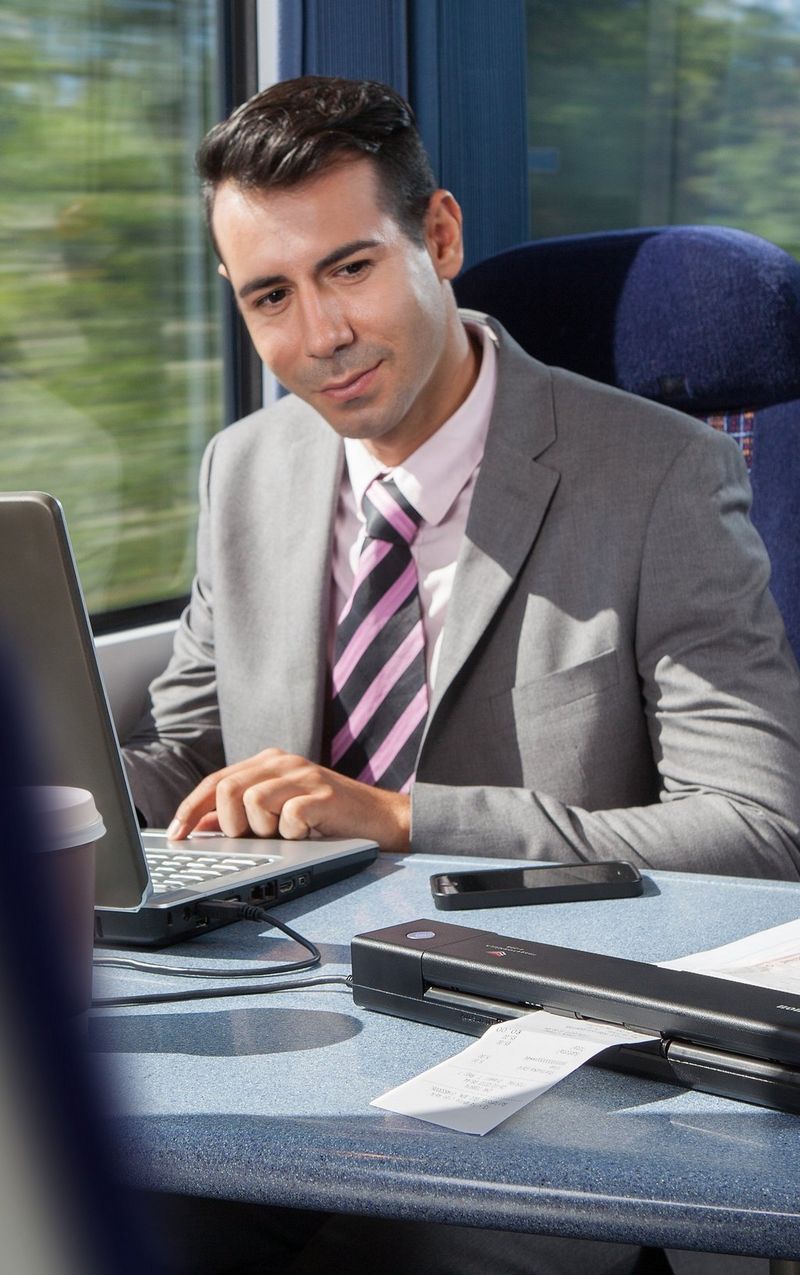 Woman with dark hair and glasses, wearing a light grey jacket and light blue shirt, smiles while using a tablet device.