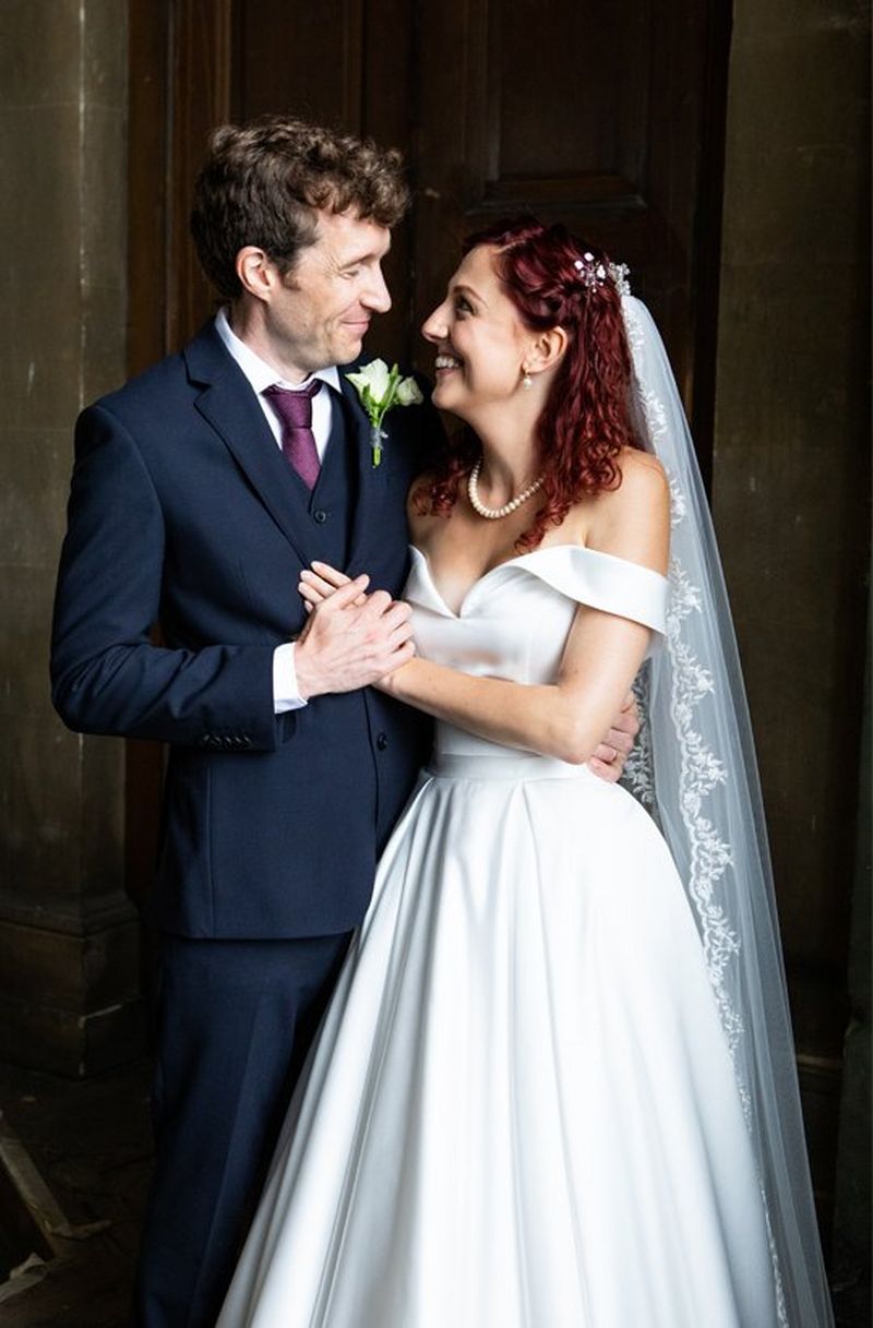 Newlyweds with their arms around each other, look into each others eyes and smile. 