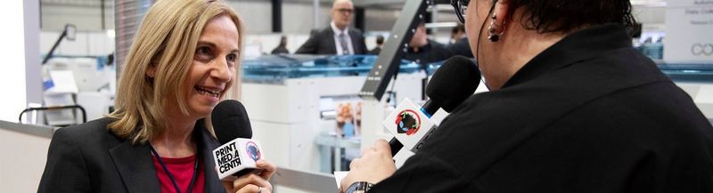 Two women speaking into microphones with ‘print media centr’ and a logo on them.