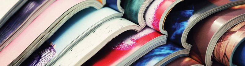 Nine magazines, open and lying on top of each other, their spines aligned from the top left of the image to bottom right.