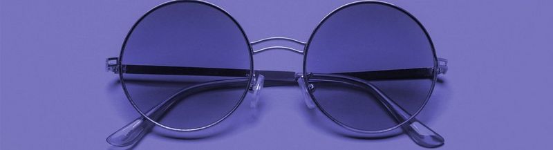 A pair of round ‘John Lennon’ style purple-tinted spectacles on a purple background.