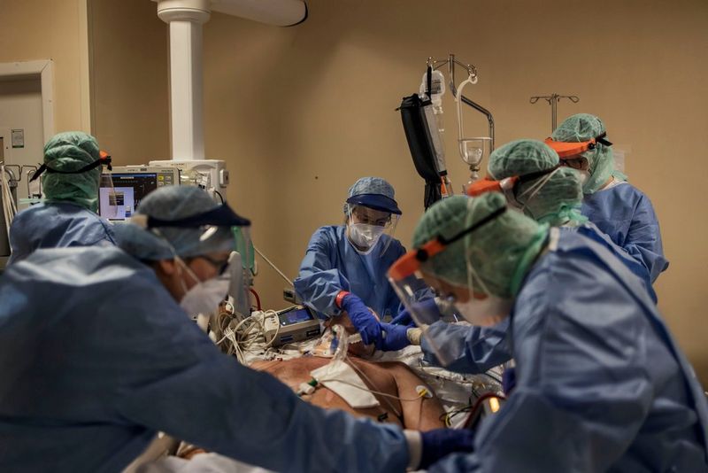  A team of nurses in protective clothing intubate a patient on a hospital bed. Photo by Fabio Bucciarelli.